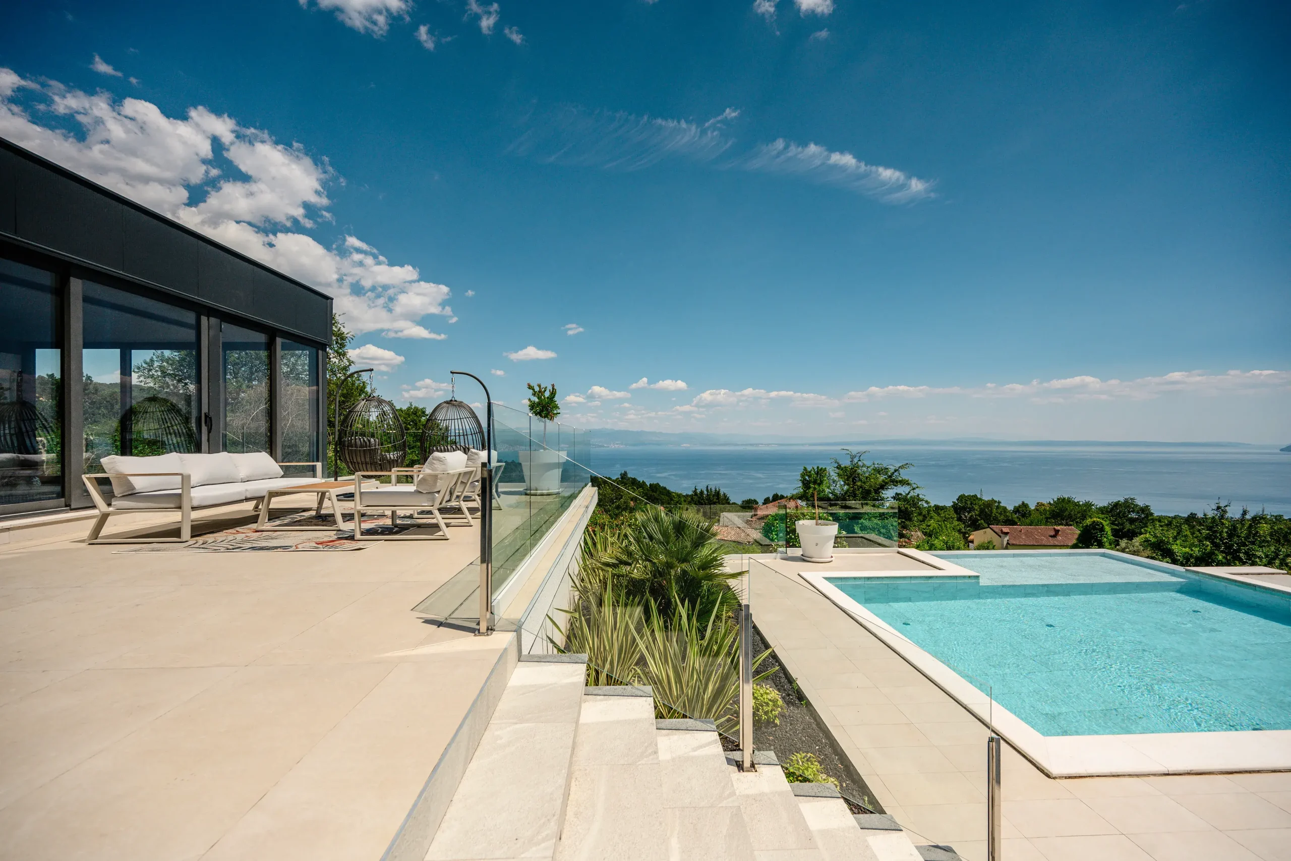 Villa Theodor terrace with hanging egg chairs, outdoor sofa and glass balustrade overlooking the Adriatic Sea