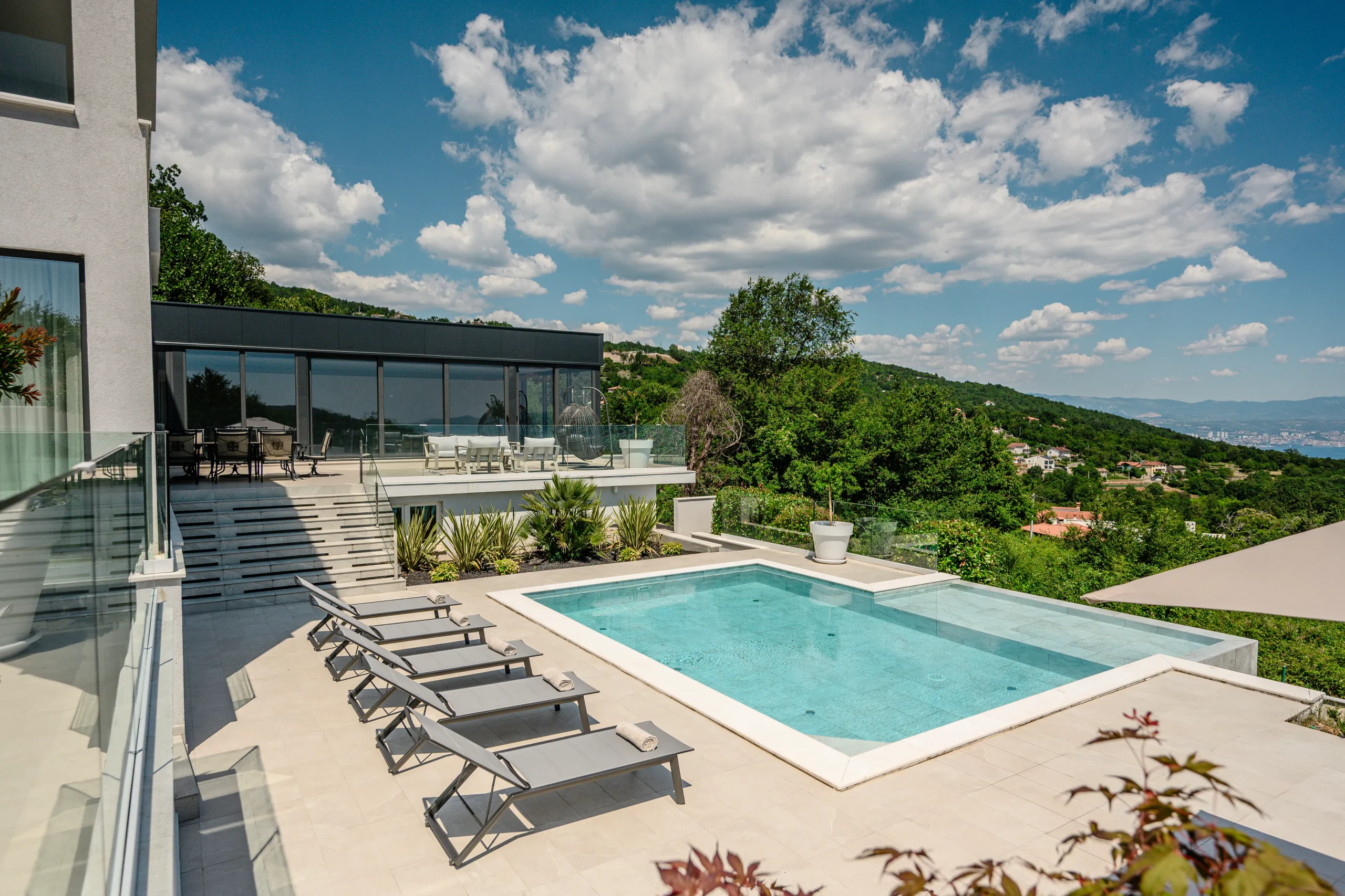 Villa Theodor's pool terrace with sun loungers framed by lush hillside greenery and village views