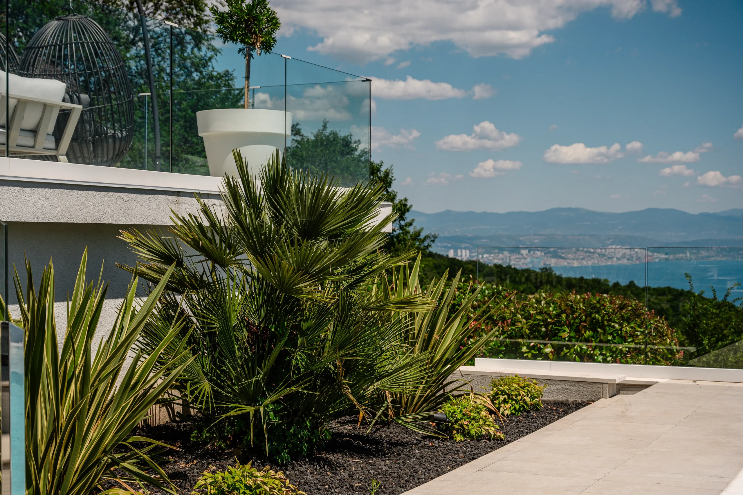 Close-up of palm and agave planting along Villa Theodor's terrace with sea and coastline views beyond