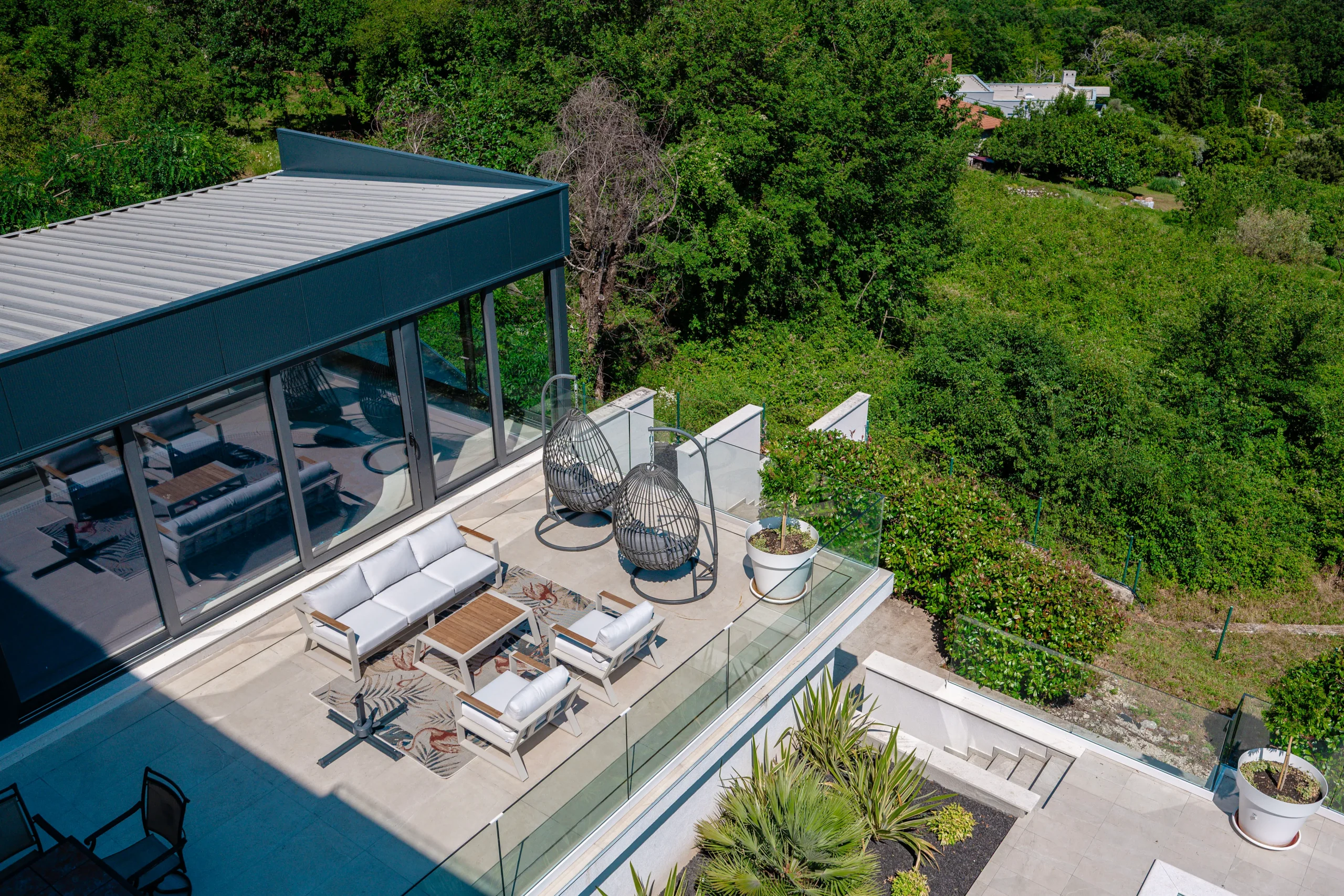 Aerial view of Villa Theodor's rooftop lounge terrace with egg chairs surrounded by forested hillside