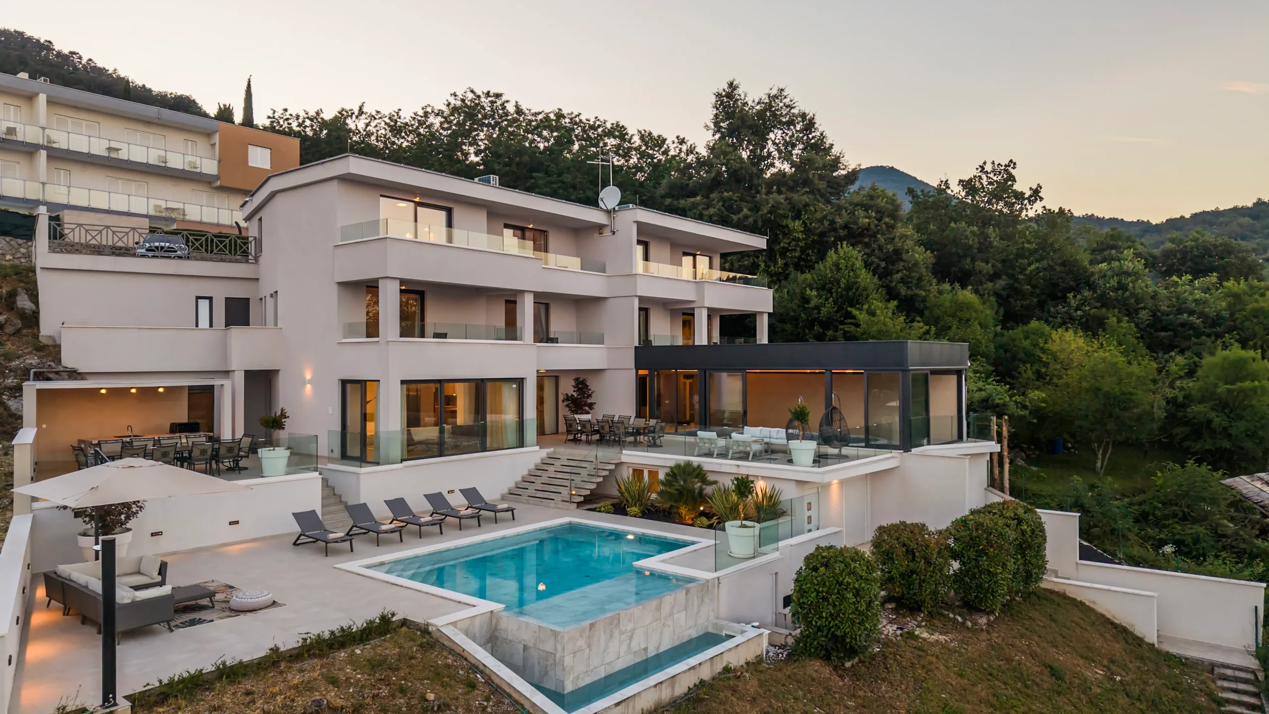 Villa Theodor's illuminated exterior and pools at dusk surrounded by dense forest hillside
