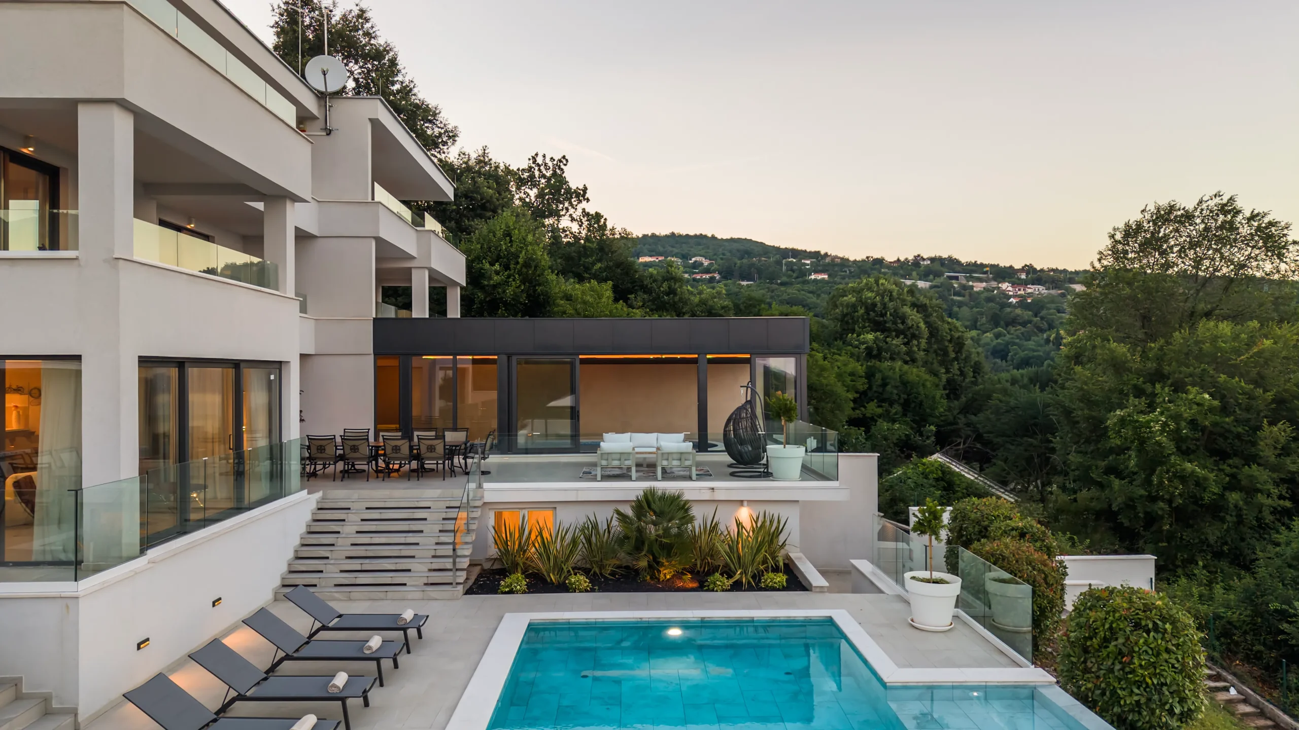Villa Theodor's dining terrace at dusk with an egg chair and forested hillside backdrop