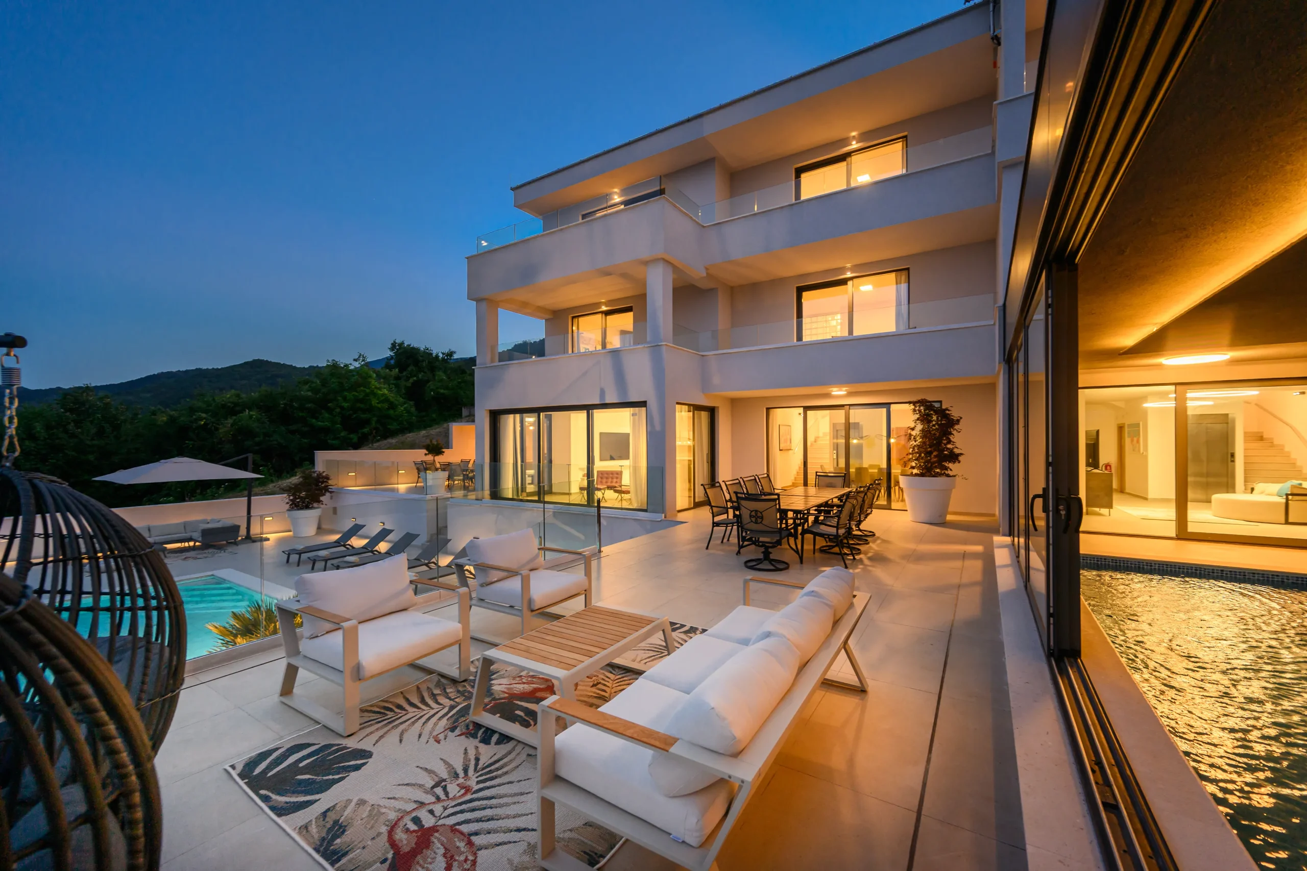 Villa Theodor's terrace lounge and illuminated pool during the blue hour with hillside views