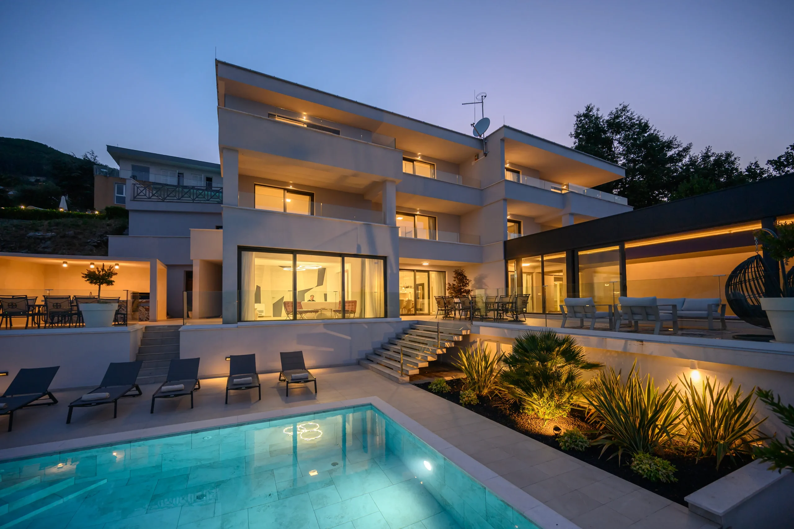 Villa Theodor's three-story exterior illuminated at dusk with pool and terrace in the foreground